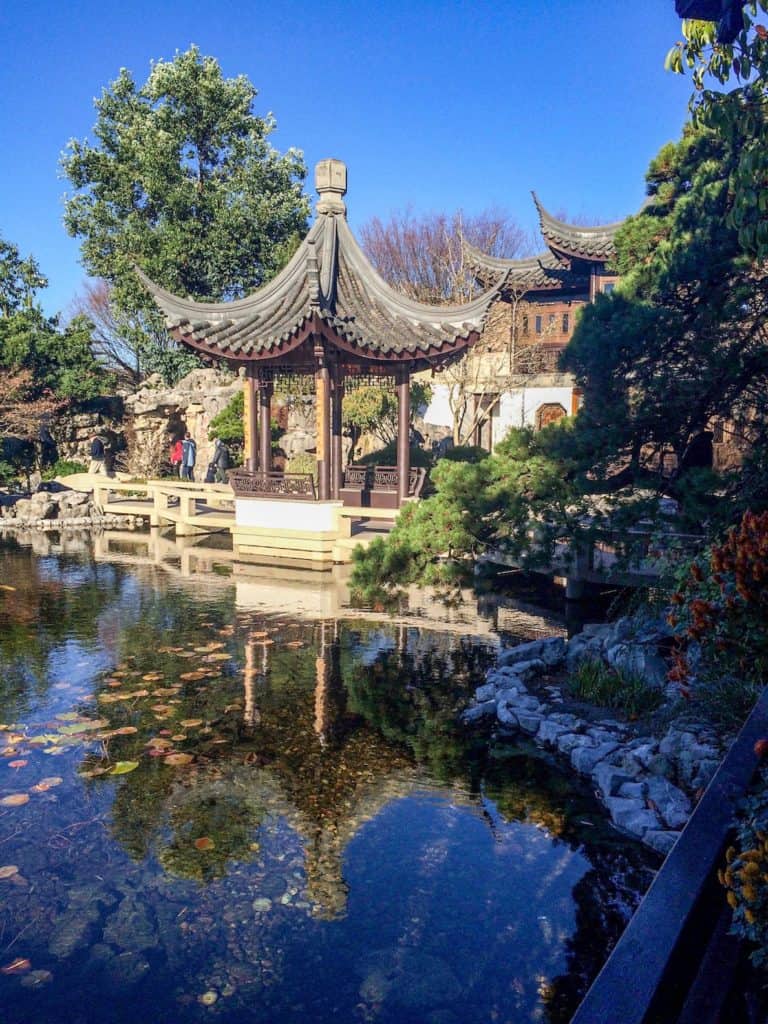 Traditional Chinese temple with intricate curved roof next to pond surrounded by Chinese Gardens. Lan Su Chinese Garden, downtown Portland, Oregon. Best things to do in downtown Portland.