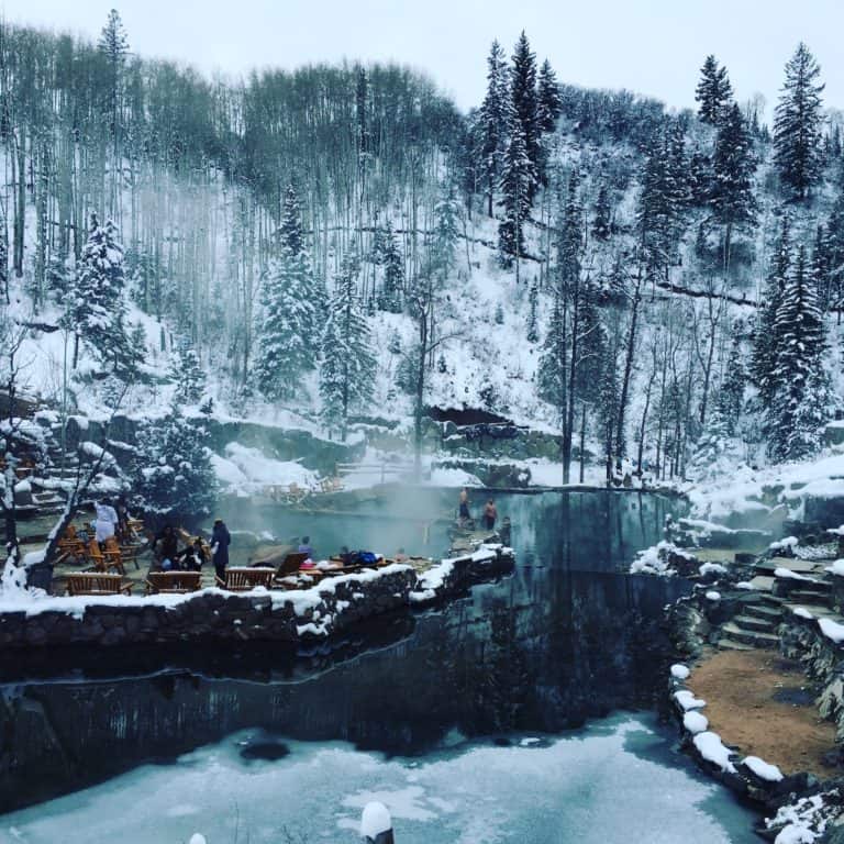 Snow covered mountainside overlooking steaming hot springs dotted with people on gloomy winter day. Strawberry Hot Springs, Steamboat Springs, Colorado.