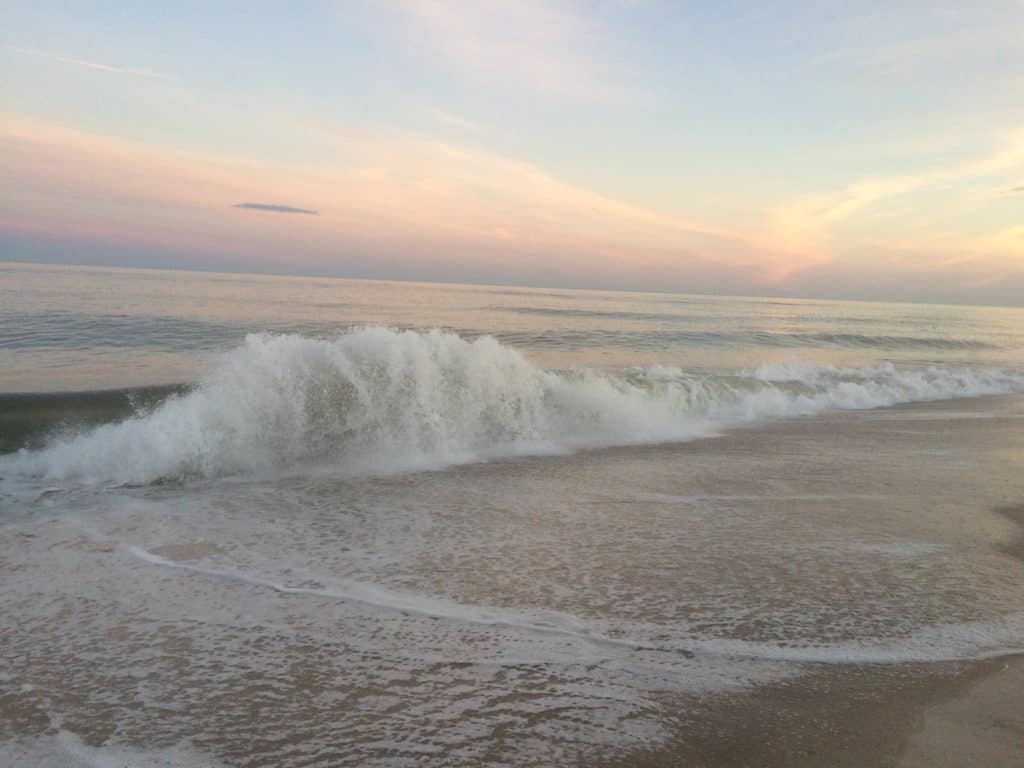 Pastel colored sunset behind waves crashing on beach. Atlantic Ocean, Sagg Main Beach, Sagaponack, New York, The Hamptons.