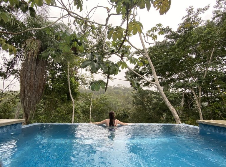 Woman with back to camera overlooking lush green jungle from beautiful private infinity pool. Infiniti pool at private suite at Lodge At Chaa Creek, San Ignacio, Belize.