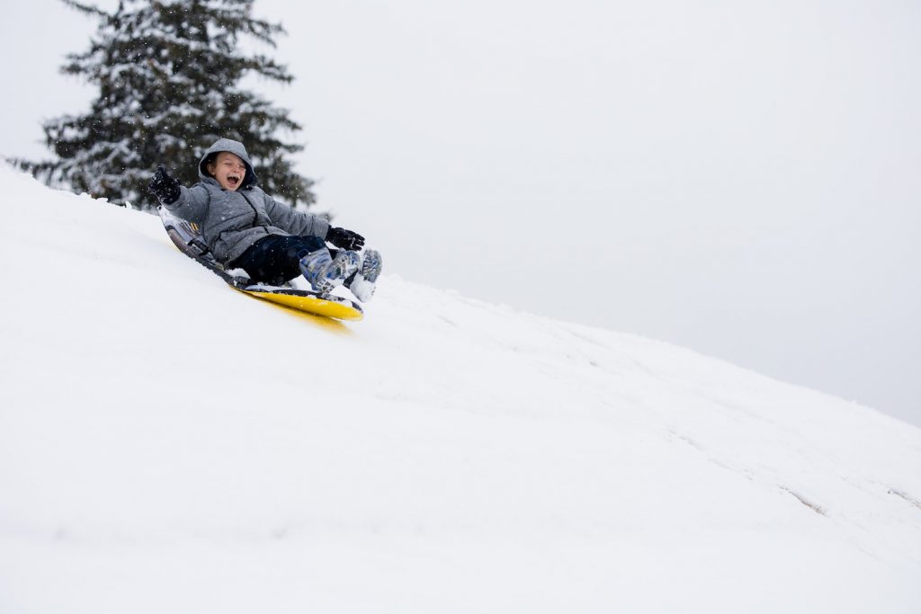 kid-laughing-and-sledding-down-snow-covered-hill-colorado-christmas