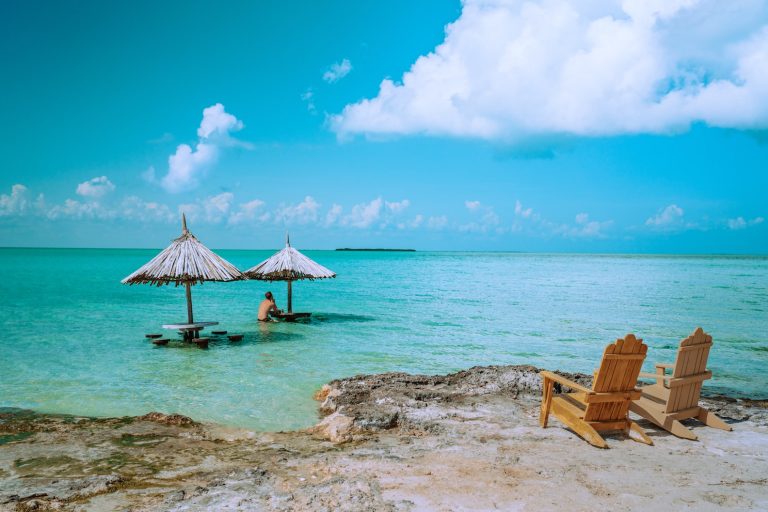 Wooden Adirondack chairs overlooking two submerged tables in bright blue water of Caribbean Sea. Secret Beach, Ambergris Caye, Belize.
