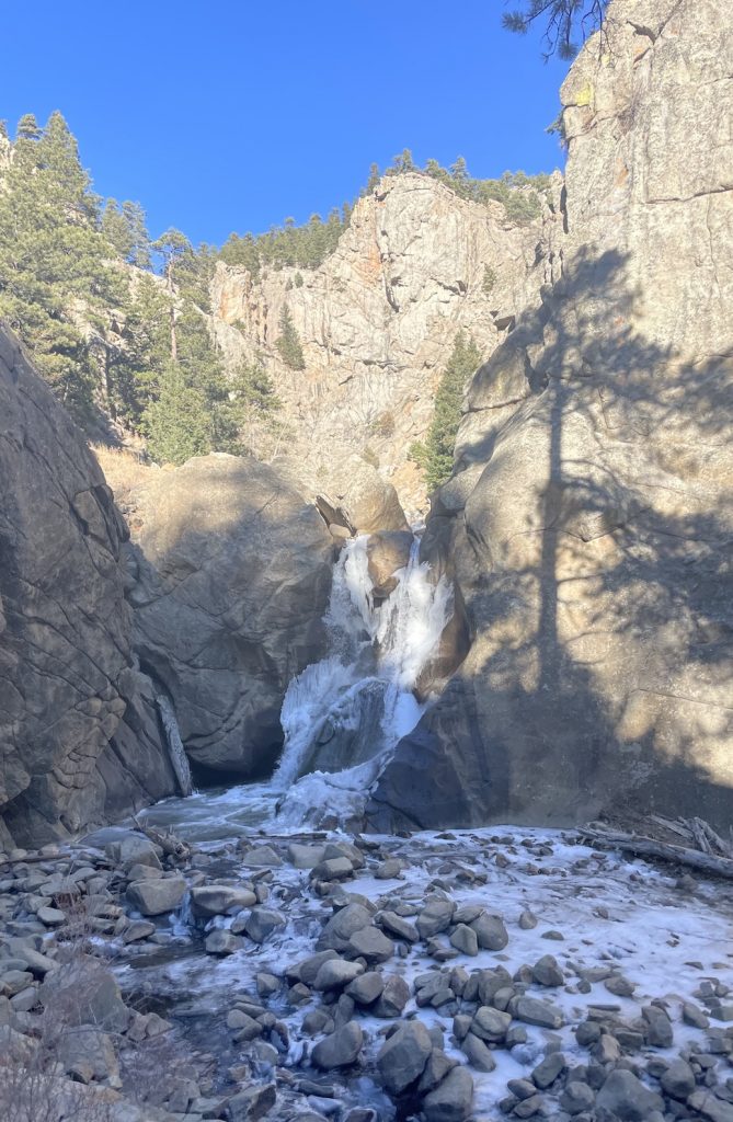 frozen waterfall surrounded by rocky cliff and pine trees during a sunny winter day. Boulder Falls, Boulder, Colorado. 24 hours in Boulder.