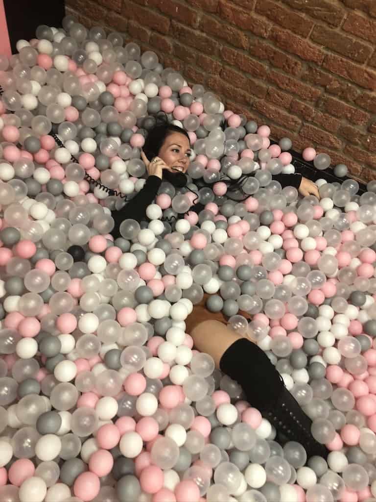 Woman smiling and pretending to be on phone in colorful ball pit at Denver Selfie Museum. Denver Selfie Museum, LoDo, Denver, Colorado.