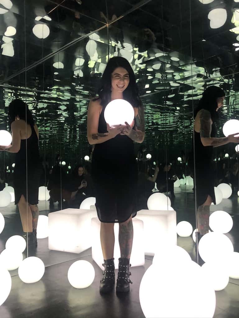 Woman holding glowing ball and laughing in dark, mirrored room with glowing balls at Denver Selfie Museum in Denver, Colorado