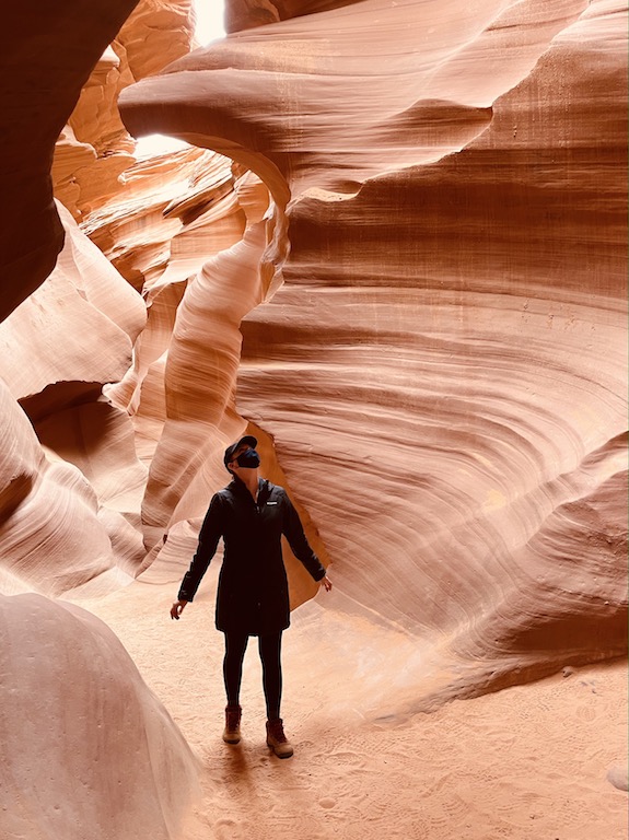 Woman standing in tall red and orange sandstone slot canyon, Lower Antelope Canyon, Page, Arizona.