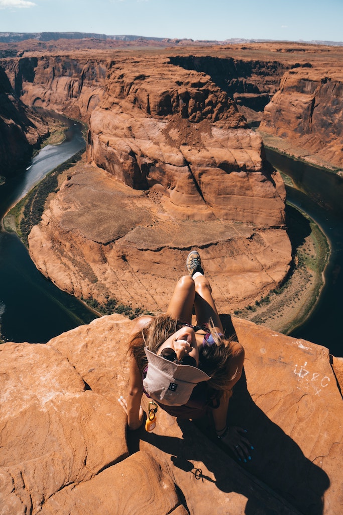 Woman smiling at camera at overlook of dramatic horseshoe shaped bend in red rock landscape. Horseshoe Bend, Page, Arizona.