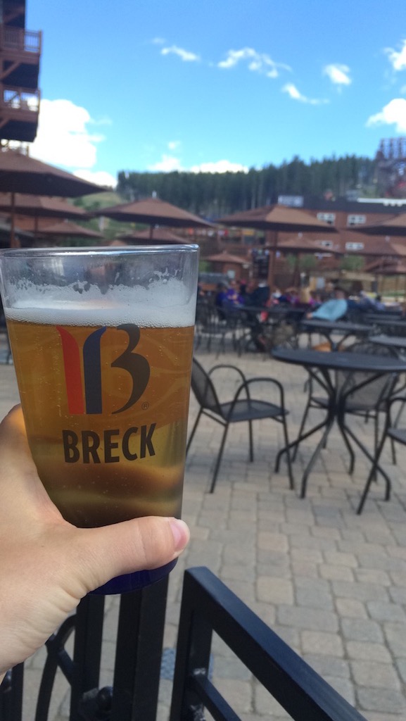 Woman holding beer with Breckenridge Ski Resort Logo on restaurant deck in Breckenridge Ski Resort during summer in Colorado Rocky Mountains