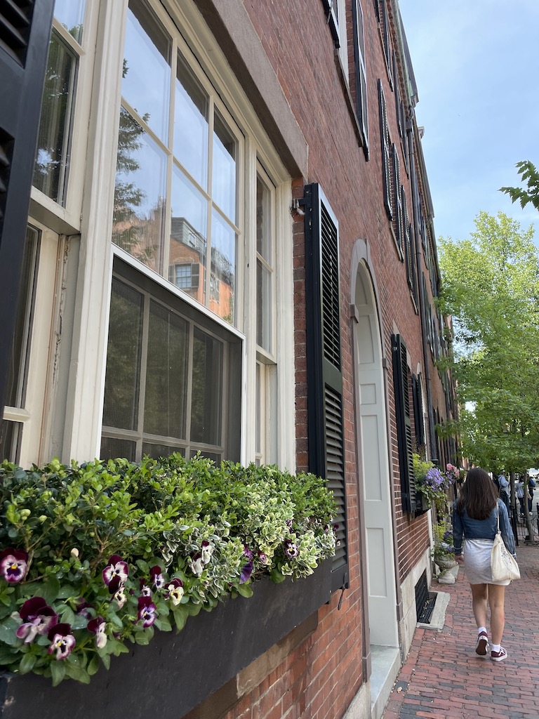 Woman walking down brick sidewalk next to historic brick homes on sunny summer day. Beacon Hill, Boston, Massachusetts, New England.