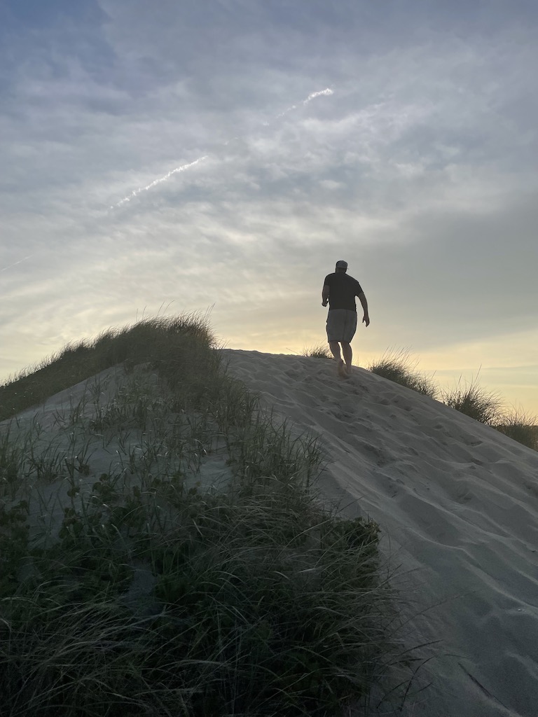 Silhouette of man running up sand dune surrounded by American beach grass during sunset. First Encounter Beach, Eastham, Massachusetts, Cape Cod.
