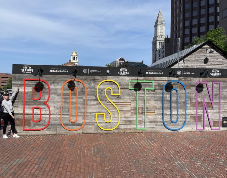 Woman next to large wooden sign with colorful letters reading "BOSTON". Boston, Massachusetts, New England.