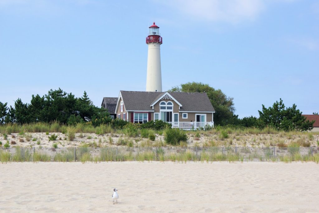 White lighthouse with white sand beach in foreground on sunny day. Cape May, Lighthouse, Cape May, New Jersey