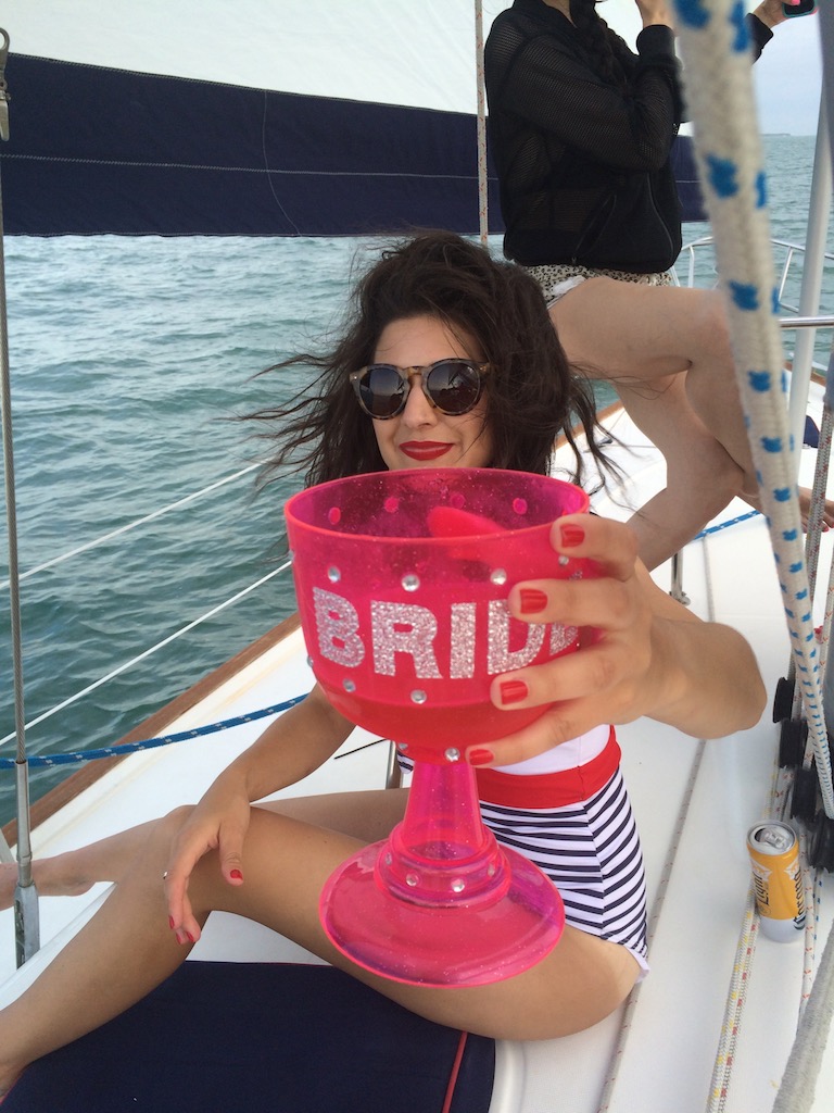 Woman on sailboat holding large pink chalice reading "BRIDE". Miami, Florida Bachelorette Party.