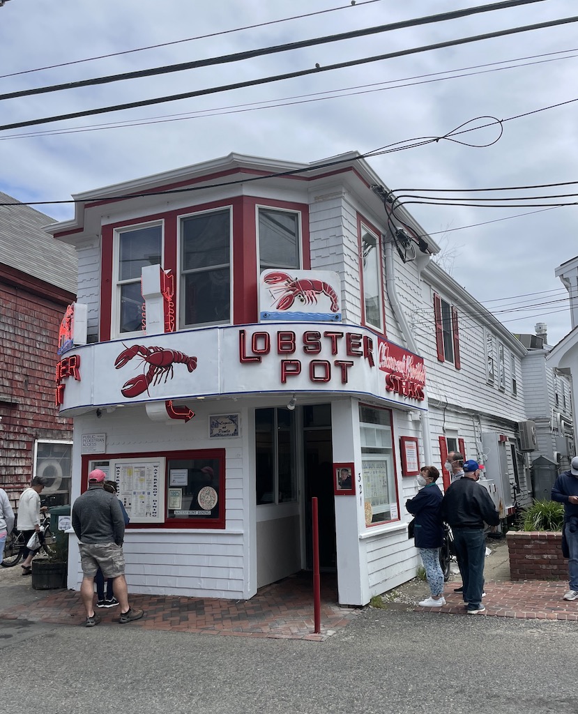 Small white building with large lobsters on it and old, neon sign reading "LOBSTER POT" with people out front waiting for food. Lobster Pot, Provincetown, Cape Cod, Massachusetts, New England.