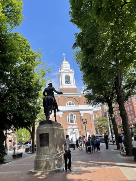 Large statue of man on horse on wide walkway with brick church in background on sunny summer day. Paul Revere Mall, Old North Church, North End, Boston, Massachusetts, New England.