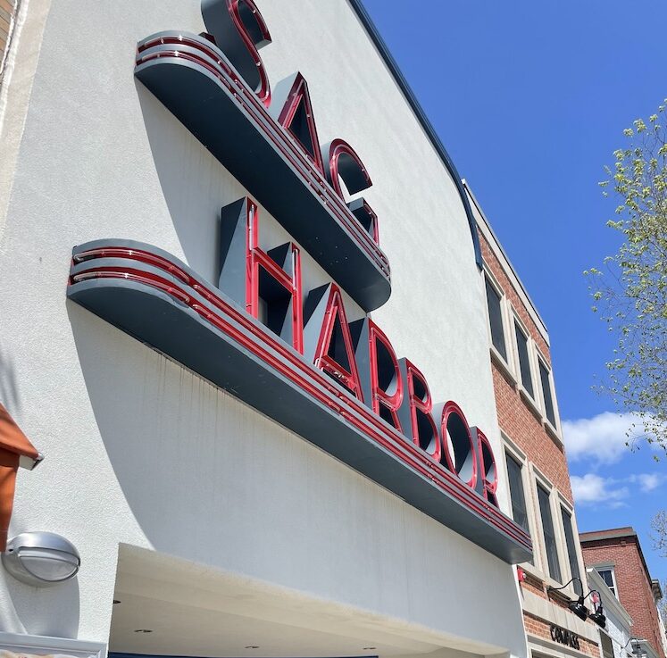 Large white building with huge red neon sign reading "Sag Harbor". Sag Harbor Cinema, Sag Harbor, New York, the Hamptons.