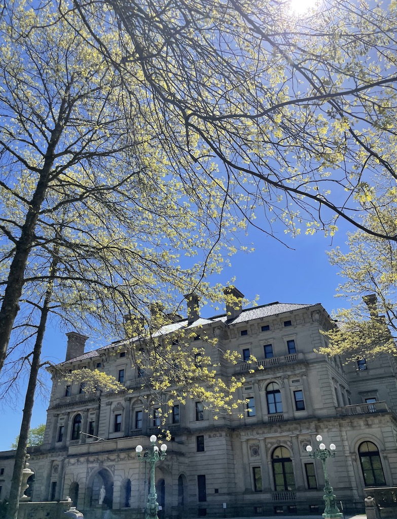 Large stone mansion with budding tree in foreground on sunny spring day. The Breakers Mansion, Newport, Rhode Island.