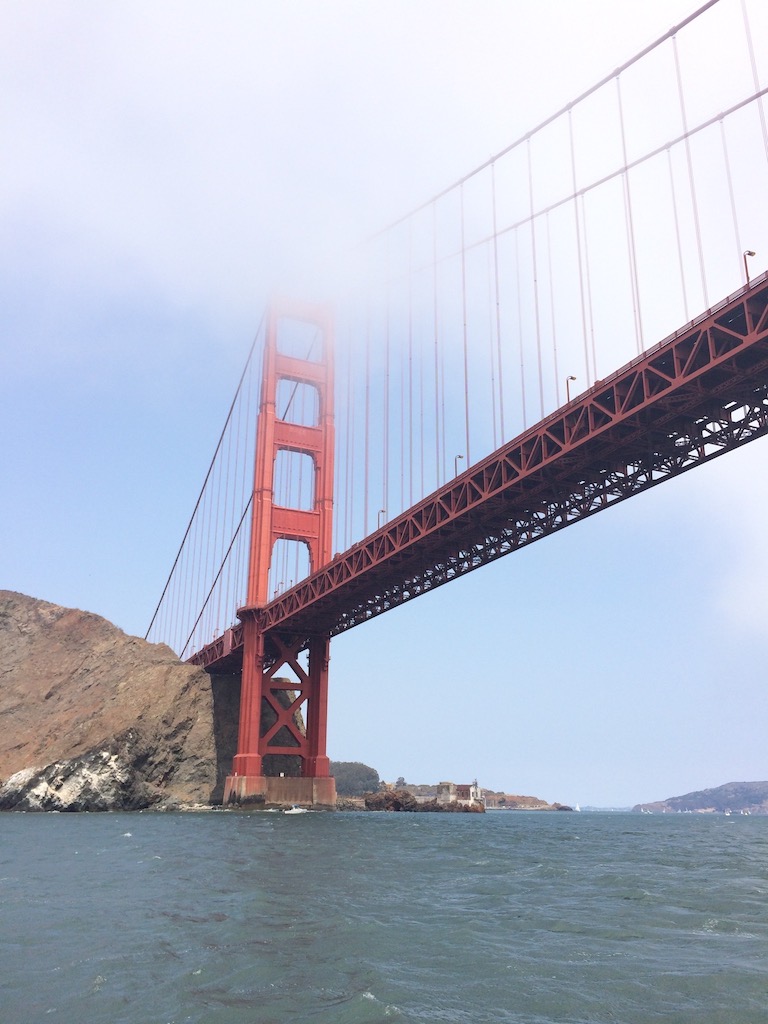 The red painted Golden Gate Bridge as seen from a boat below, with a little fog covering the top. San Francisco Bay, San Francisco, California. 1 Day in San Francisco itinerary.