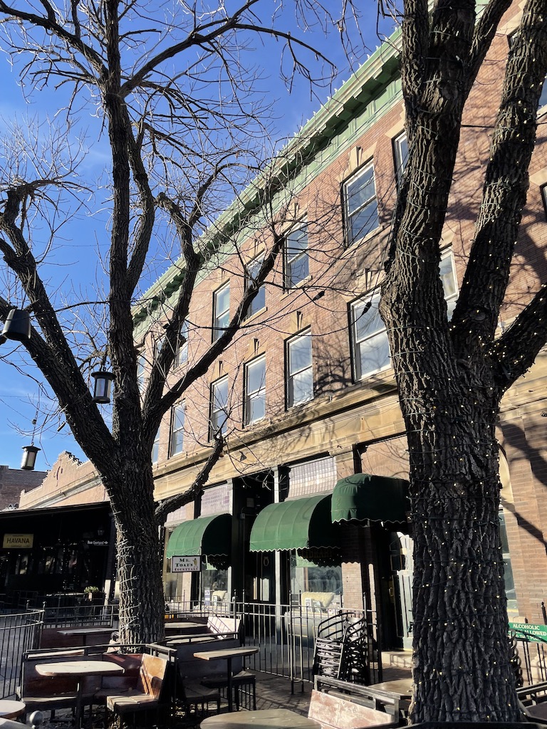 Brick building overlooking courtyard with outdoor seating and bare winter trees. Old Market, Omaha, Nebraska.