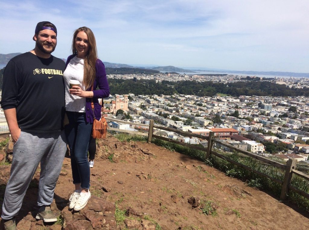 Man and woman smiling at camera with views of San Francisco and San Francisco Bay in distance. Grandview Park, San Francisco, California.