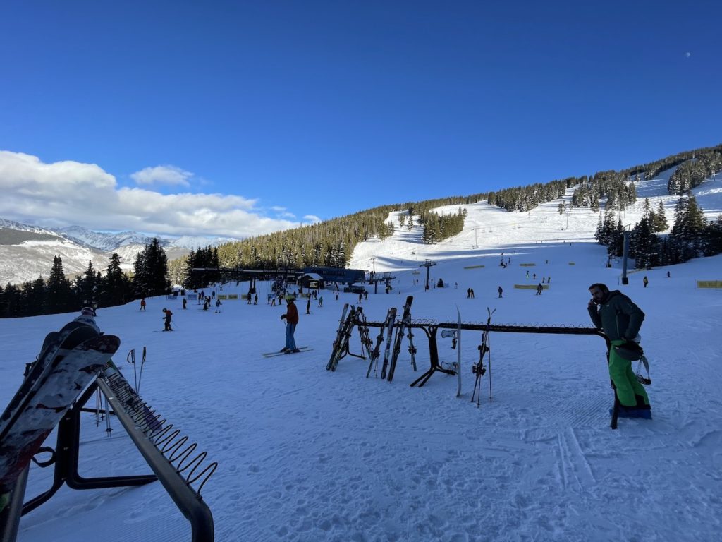 Ski racks atop ski slopes on sunny winter day, skiers and snowboarders in distance. Vail Ski Resort, Vail Mountain, Vail, Colorado.