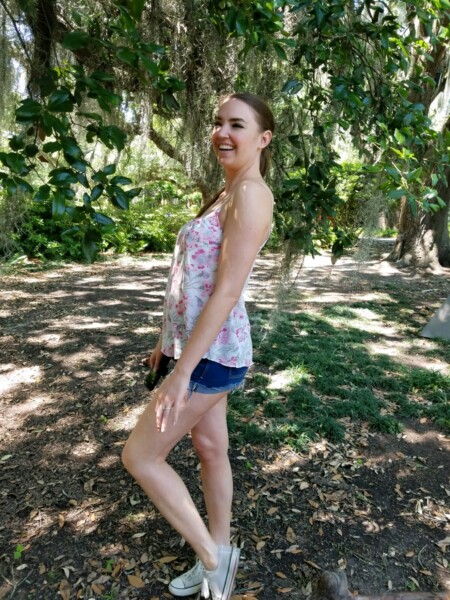 Woman smiling in lush green park under a live oak tree during summer. Besthoff Sculpture Garden, New Orleans Museum of Art, New Orleans, Louisiana.