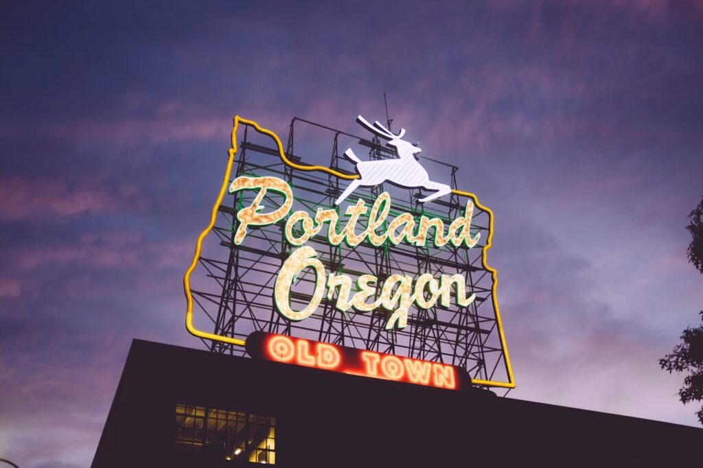 Dark blue sky with pink clouds during sunset, foreground is large lit sign with white horse and text reading "portland oregon old town" Downtown, Portland, Oregon. Free things to do in Portland.