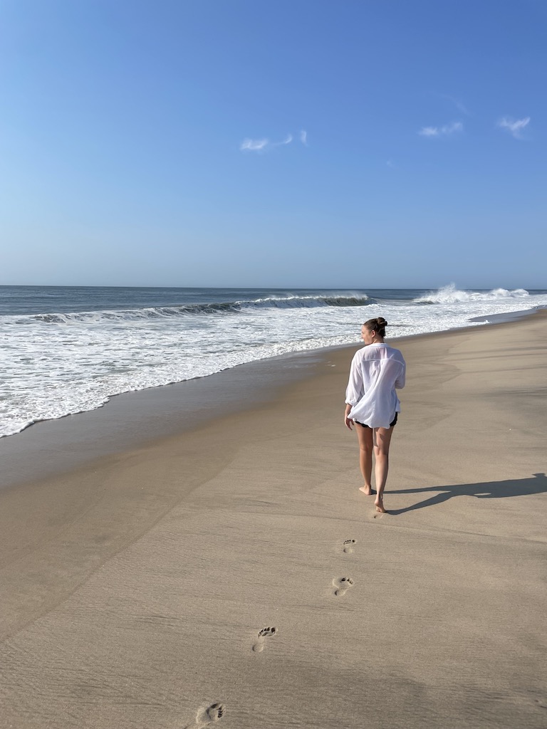 Woman walking down white sand beach along Atlantic Ocean. Sagg Main Beach, Sagaponack, New York, The Hamptons.