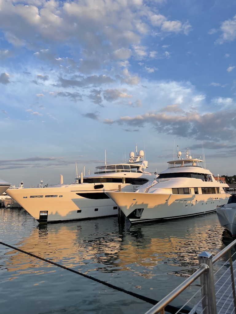 Two huge, white yachts docked on calm harbor water on sunny summer evening. Sag Harbor Yacht Yard, Sag Harbor, New York, The Hamptons.