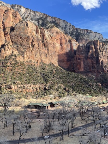 Ariel view of red rock cliffs rising out of canyon floor with small parking lot, road and lodge at bottom of canyon. Zion National Park Lodge, Zion National Park, Utah.