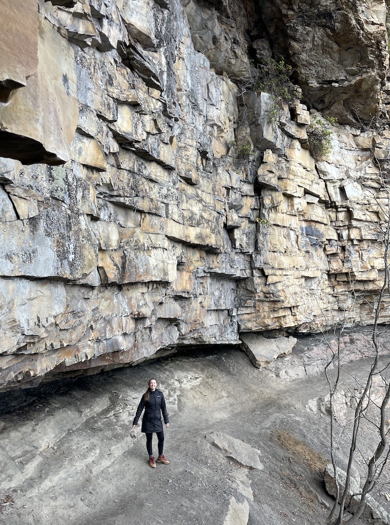 Woman standing under rocky cliff on hiking trail in fall. Castle Rock Trail, New River Gorge National Park, West Virginia.