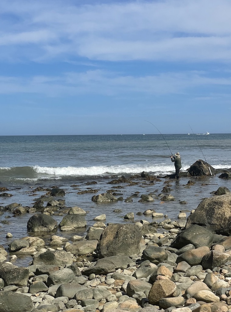 Man fishing in rocky Atlantic Ocean shoreline. Montauk Point State Park, Montauk, New York, The Hamptons.