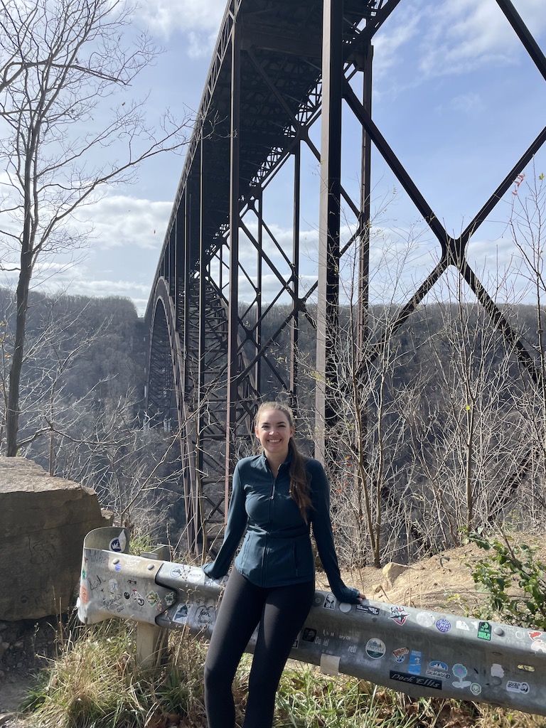 Woman standing under huge steel bridge. Fayette Station Road, New River Gorge Bridge, New River Gorge National Park, West Virginia.