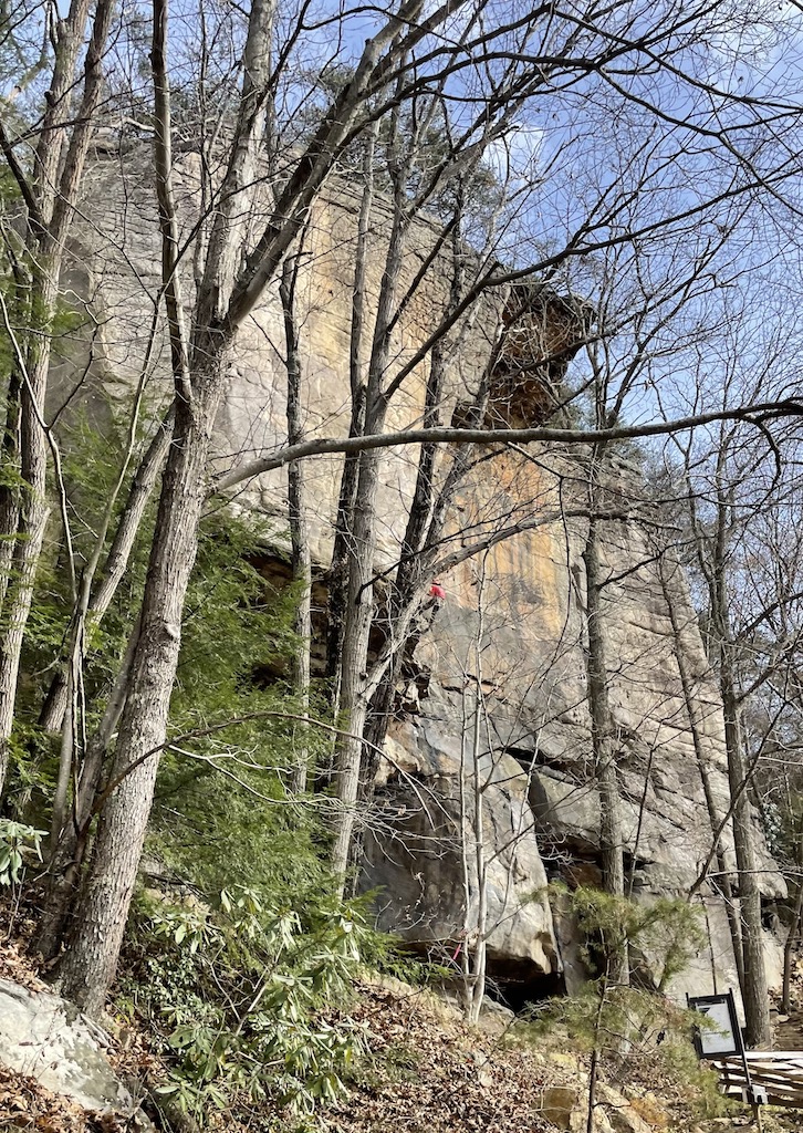 Rock climber on huge rocky cliff on sunny winter day. New River Gorge National Park, West Virginia.