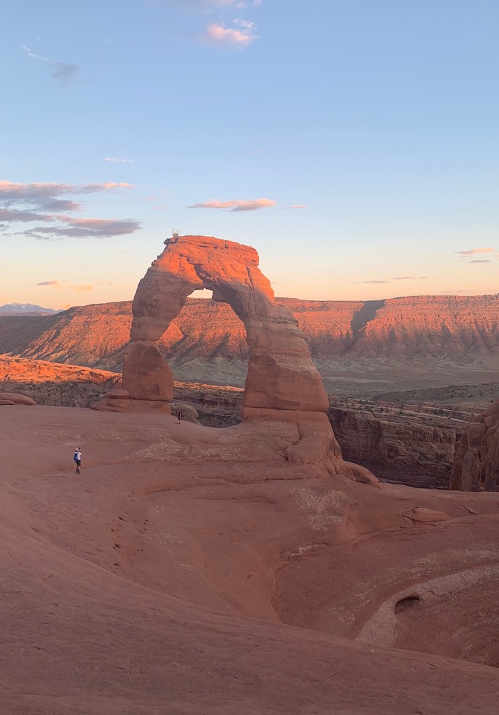 Huge free standing arch of red rock with red rock landscape in background at sunset. Delicate Arch, Arches National Park, Utah.