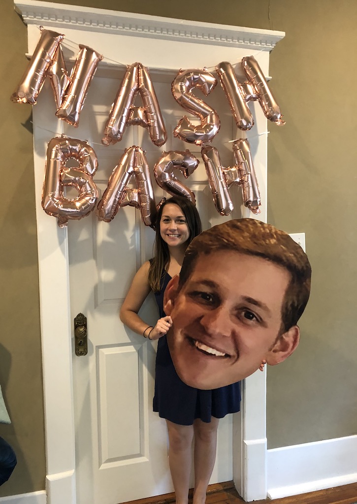 Woman smiling and holding large cut out printing of mans head, man is smiling. Pink balloon letters hang in background and read "NASH BASH" Bachelorette party, Nashville, Tennesse.