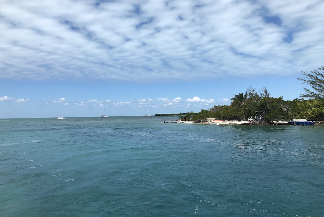 Bright blue water of the Caribbean Sea with lush green island and sailboats in distance on sunny day. Caye Caulker, Belize.