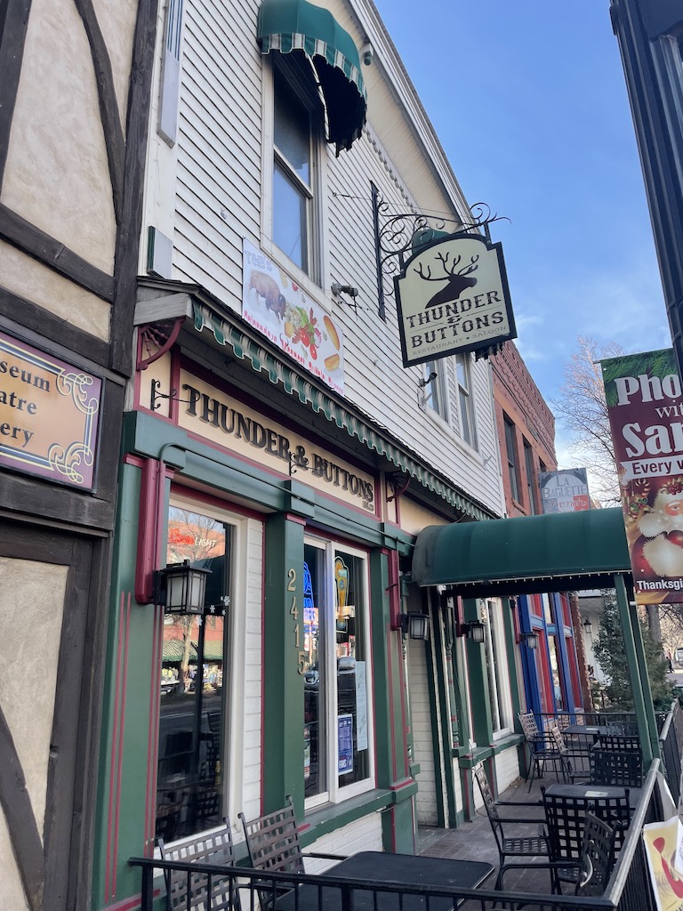 Wooden, mining-boom era styled building with green awning and outdoor patio seating, sign extends from building with elk and text reading "thunder & buttons". Old Colorado City, Colorado Springs, Colorado.