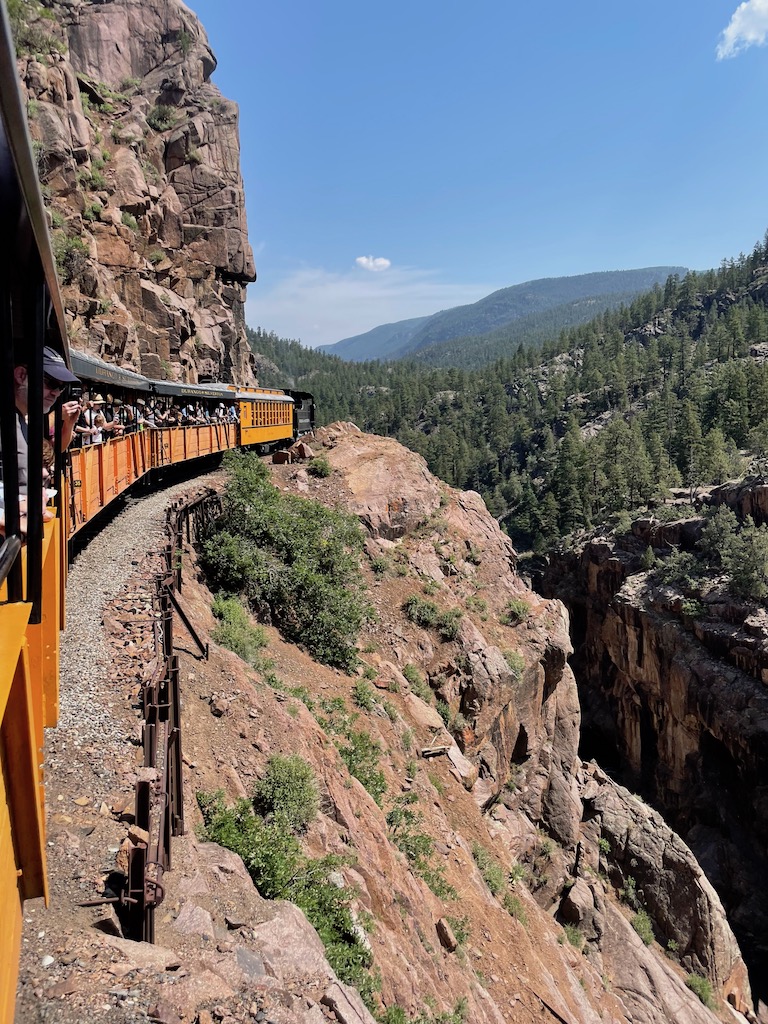 Steam engine train winding through mountains along rocky cliff edge on sunny summer day. Durango Silverton Train, Rocky Mountains, Durango, Colorado.