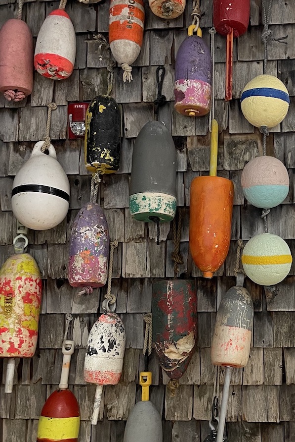 Colorful lobster buoy's hanging from grey shingled buildiing.
