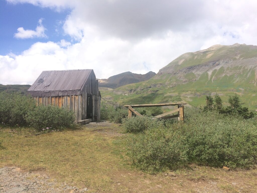Old wooden cabin deterorating after being abandoned long ago surrounded by gorgeous mountain views on sunny summer day. Ghost town/ old mining town, Blue Lakes Trail, San Juan Mountains, Telluride, Colorado.