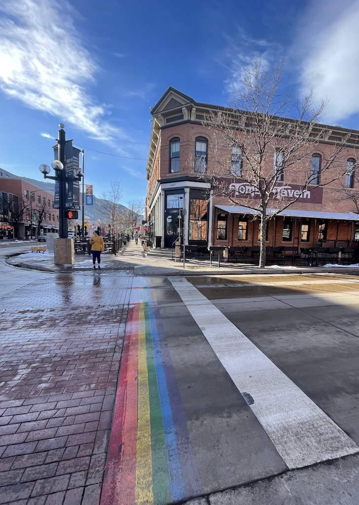 Small rainbow path leading across street to large brick building on sunny winter day. Pearl Street Mall, Boulder, Colorado.