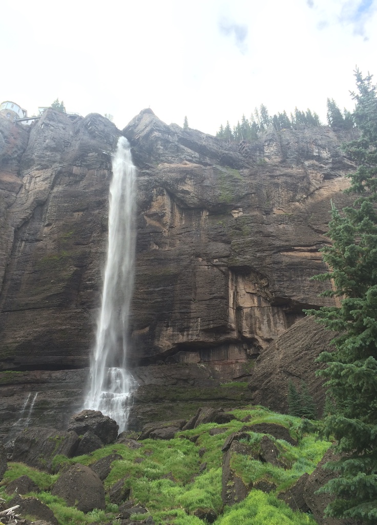 300 foot free falling waterfall with sheer rock face on either side and moss covered rocks below. Bridal Veil Falls waterfall, San Juan Mountains, Telluride, Colorado.