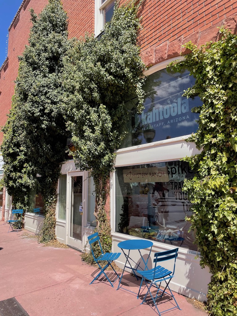 Blue bistro tables set outside in front of brick building covered in ivy on bright sunny day. Heritage Square, Downtown Flagstaff, Arizona. Flagstaff what to do.