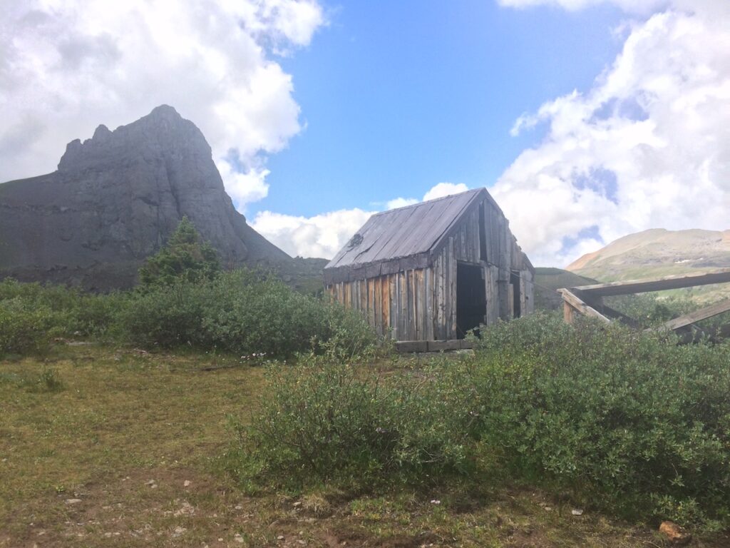 Abandoned wooden cabin/ home near abandoned mining area with rocky mountain peak in background on sunny summer day. Blue Lakes Trail, San Juan Mountains, Telluride, Colorado.