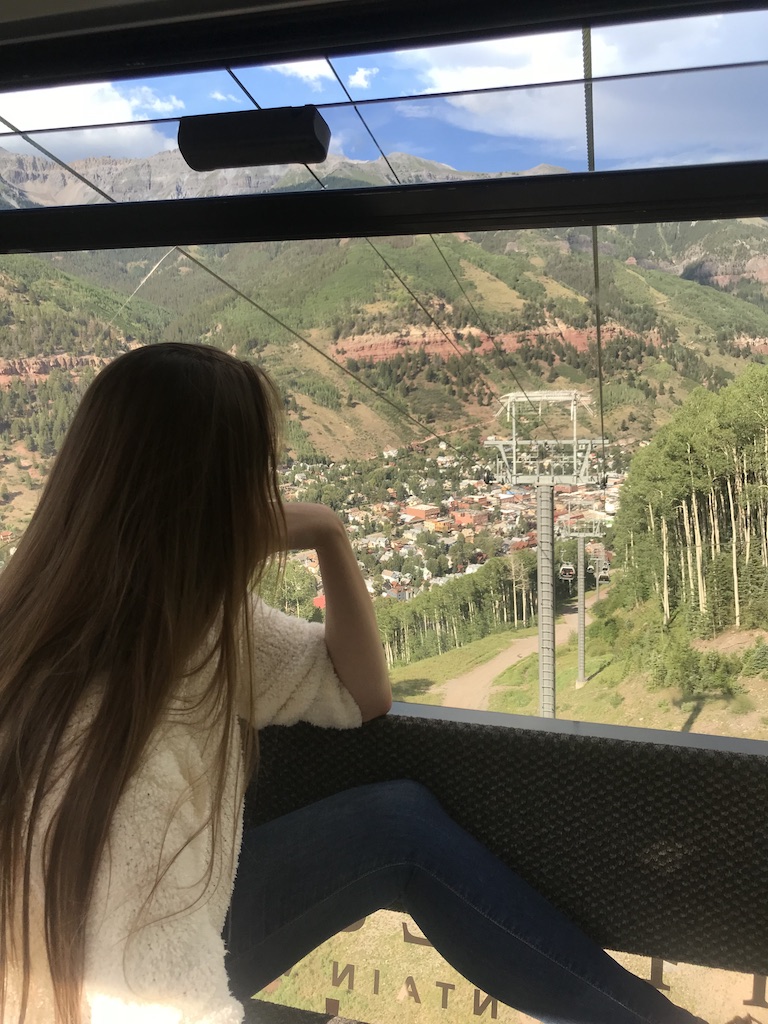 Woman looking out window of gondola as it descends into the town of Telluride on sunny summer afternoon. Telluride Gondola, Telluride, Colorado.