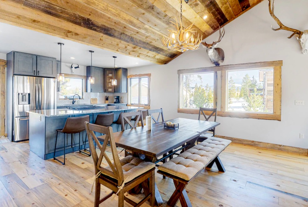 Luxury kitchen with large island, dining room table, antler chandelier, buck head on wall, spacious vaulted ceilings, and new, modern appliances and finishes. Cabins at Grand Lake, Colorado.
