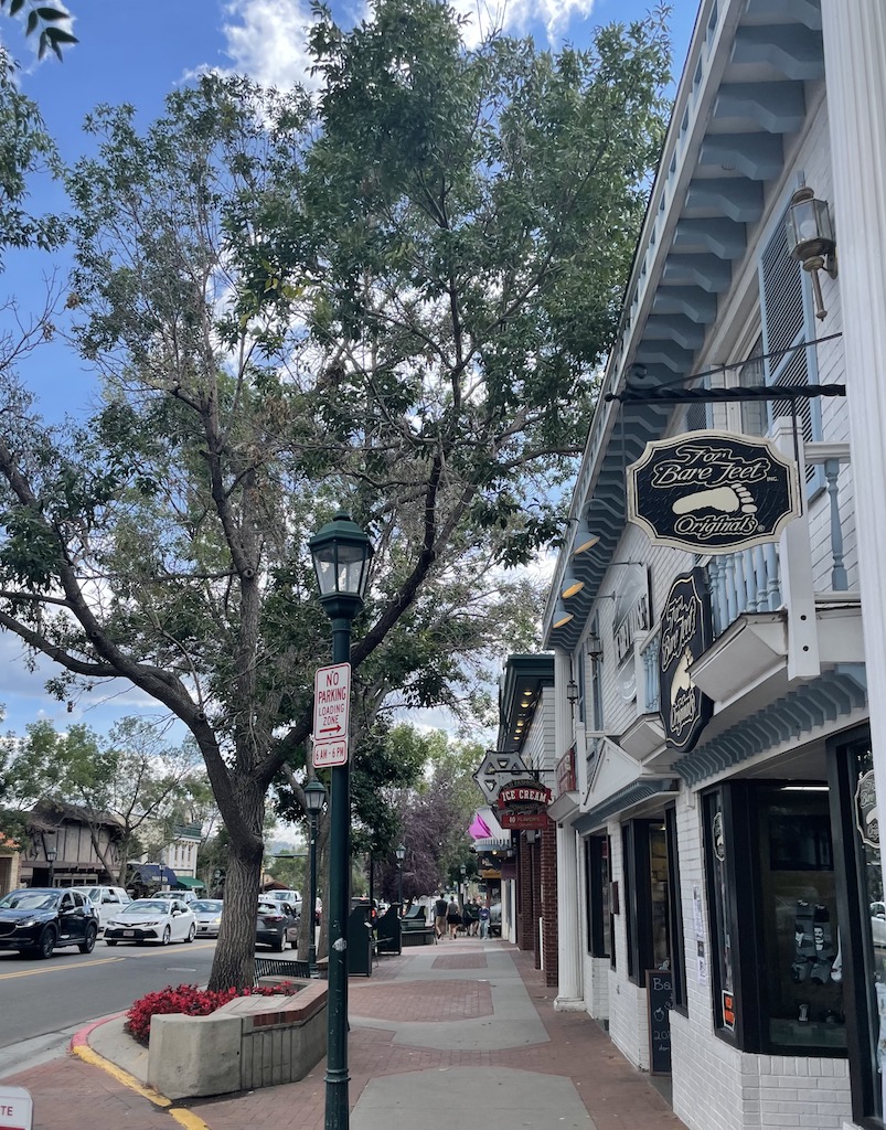 Tree-lined pedestrian walkway lined with small boutique and souvenir shops in charming buildings on sunny summer day. Shopping in downtown Estes Park, Colorado.