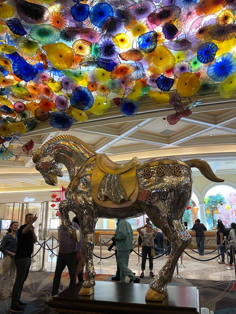 People looking at large horse statue in silver and gold under huge colorful glass sculpture by Dave Chihuly, Fiori di Como glass sculpture, Bellagio Hotel and Casino lobby, Las Vegas, Nevada.