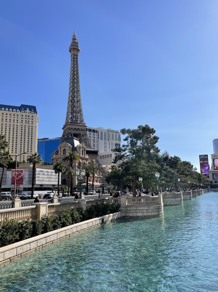 Eiffel Tower surrounded by high rise mega casino hotels and Las Vegas Strip with Bellagio Fountains in foreground on cloudless day. Paris Hotel & Casino, Bellagio Hotel & Casino, The Las Vegas Strip, Las Vegas, Nevada.